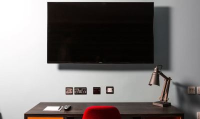 a large flat screen tv mounted on the wall above a desk with a red chair at Village Hotel Liverpool