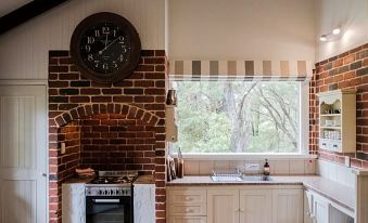 a brick oven with a clock above it is in a kitchen next to a window at William Bay Cottages