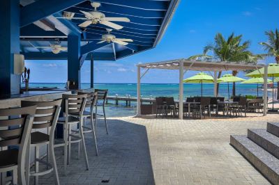 a beach scene with a bar , dining tables , and umbrellas set up on a pier near the ocean at Wyndham Reef Resort Grand Cayman