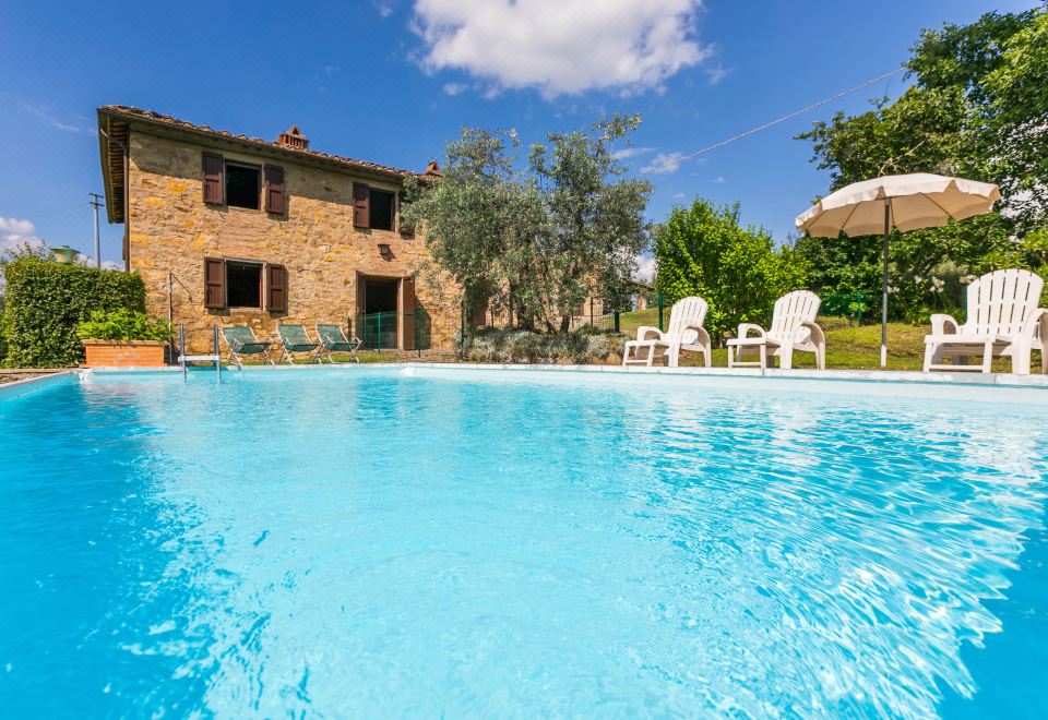 a large outdoor swimming pool surrounded by a brick house , with several chairs placed around it at Il Laghetto