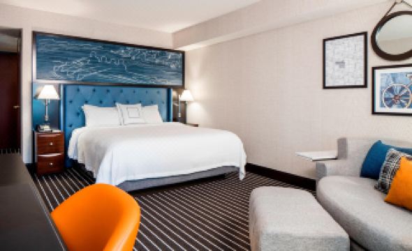 a modern hotel room with a large bed , blue headboard , and white bedding , along with a couch and chair at Courtyard Boston Brookline