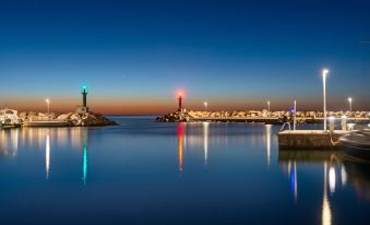 a serene nighttime view of a harbor with lighthouses and reflections in the water , illuminated by colorful lights at Hotel Cala Bona