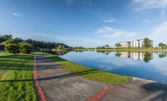 a serene landscape with a long walk way leading to a calm lake , surrounded by lush greenery and a clear blue sky at Ramsey Park Hotel