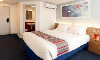 a neatly made bed with white sheets and a striped blanket is in a room with blue carpet at Travelodge Hull South Cave