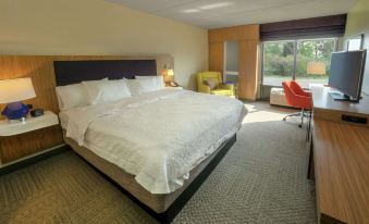 a large bed with white sheets and a headboard is in a room with a chair , lamp , and window at Hampton Inn Hazleton