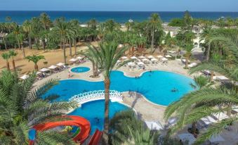 a large resort with multiple swimming pools , slides , and palm trees near the ocean , under a clear blue sky at Hotel Marhaba Beach
