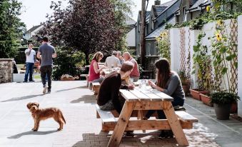 a group of people and a dog are gathered around a wooden picnic table in a courtyard at The Garret