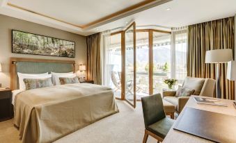 a luxurious hotel room with a large bed , a desk , and a view of the mountains outside the window at Althoff Seehotel Überfahrt