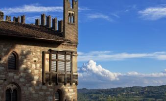 a stone building with a tower and arched windows , surrounded by trees and a blue sky with clouds at Castello di Gabiano