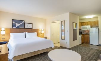 a modern hotel room with a large bed , white bedding , and a kitchenette in the background at Staybridge Suites Milwaukee Airport South