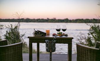a wooden dining table with two wine glasses and a candle , situated near a body of water at Old Drift Lodge