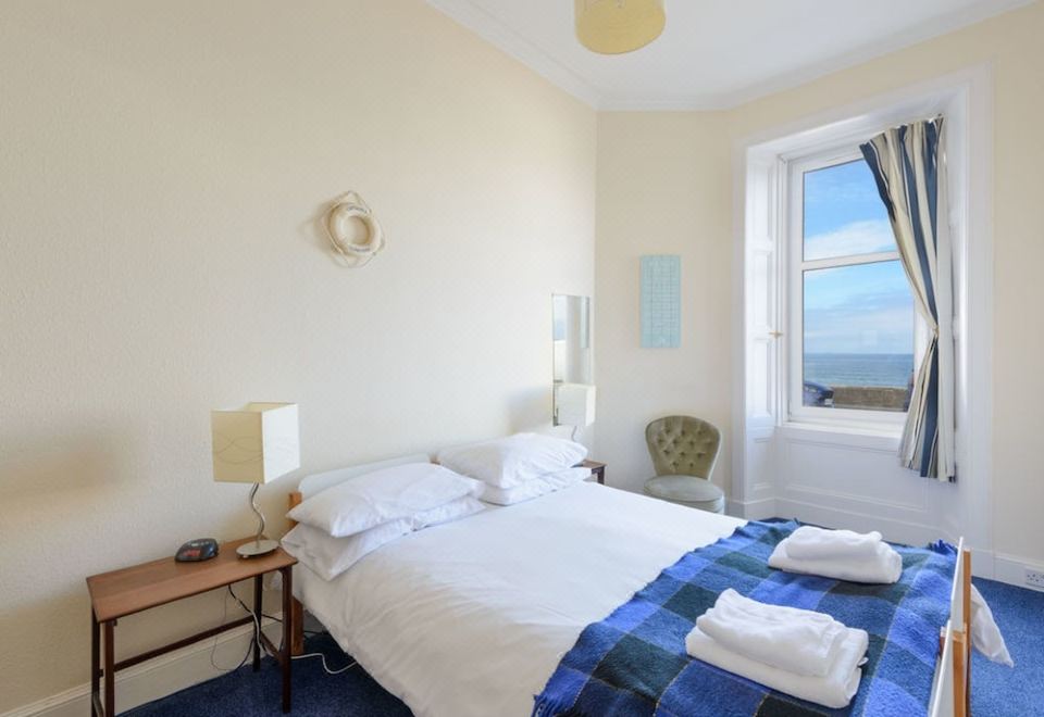 a white bedroom with a double bed , a blue and white striped comforter , and a window overlooking the ocean at Driftwood