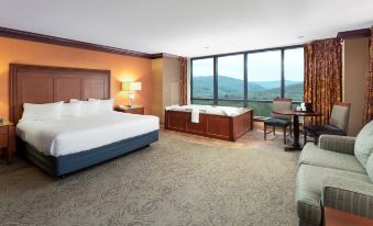 a hotel room with a king - sized bed , a bathtub , and a view of the mountains outside the window at Seneca Allegany Resort & Casino