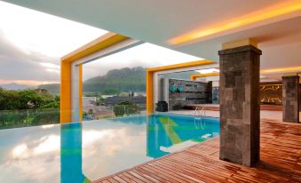 an outdoor pool with a large , blue and yellow structure in the background , and a wooden deck with lounge chairs at Grand Artos Hotel & Convention