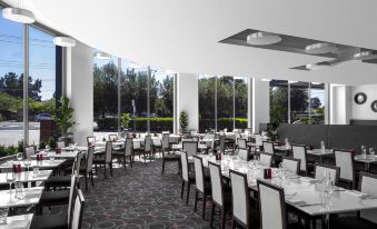 a large dining room with white chairs and tables , surrounded by windows that allow natural light to enter the space at Mantra Melbourne Airport