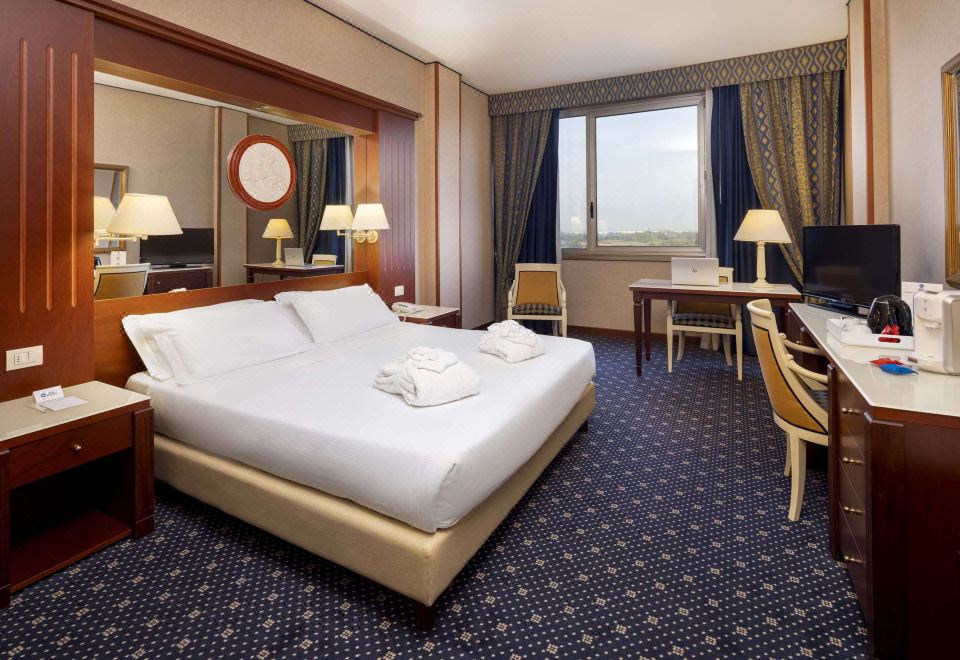 a large , well - lit hotel room with a white bed , two nightstands , and a window offering a view of the city at Best Western CTC Hotel Verona
