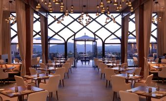 an open - air restaurant with a large glass window and white walls , allowing natural light to fill the space at Anantara Al Jabal Al Akhdar Resort