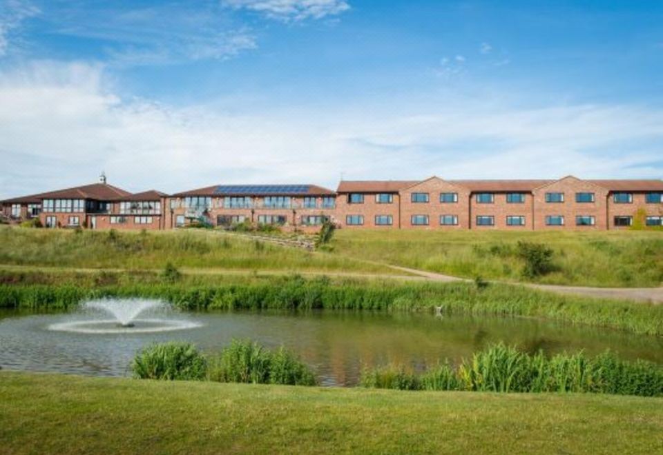 a large building with a courtyard and a pond in front of it , surrounded by grass and trees at Greetham Valley