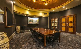 a conference room with a wooden table surrounded by chairs and a large screen on the wall at Nightcap at Matthew Flinders Hotel