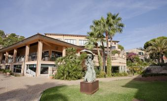 a large , modern building with a stone statue in front , surrounded by palm trees and greenery at Mon Port Hotel & Spa
