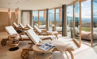 a large room with several lounge chairs arranged in a row , overlooking a beautiful view of the ocean at Alpin Panorama Hotel Hubertus