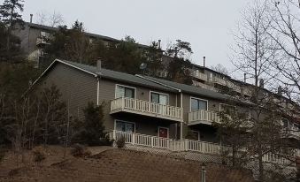a two - story house on a hillside , surrounded by trees and bushes , with a dirt road leading up to it at Creekside Village
