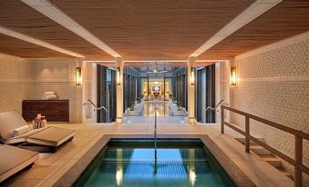 a luxurious indoor pool area with wooden ceiling , multiple lounge chairs , and white walls , under a wooden ceiling with exposed beams at Mandarin Oriental, Doha