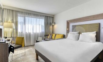 a hotel room with a large bed , couch , and desk , along with a window and curtains at Novotel Paris Nord Expo Aulnay