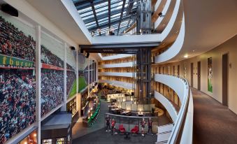 a large atrium in a modern building with a glass ceiling and high ceilings , filled with various seating areas at Lindner Hotel Leverkusen Bayarena