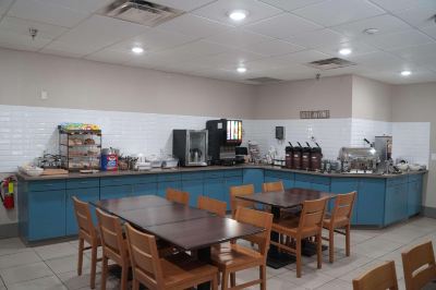 a dining area with blue cabinets and chairs , featuring a table with a tray of food and an array of bottles on the counter at Country Inn & Suites by Radisson, Watertown, SD