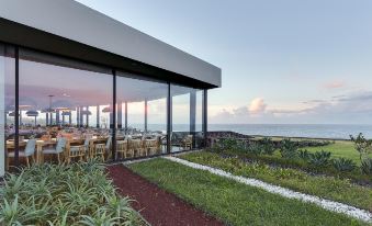 a modern restaurant with large windows overlooking the ocean , creating a serene and inviting atmosphere at Pedras do Mar Resort & Spa
