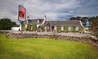 a large building with a sign in front of it and a lawn with grass at The Cock and Bull