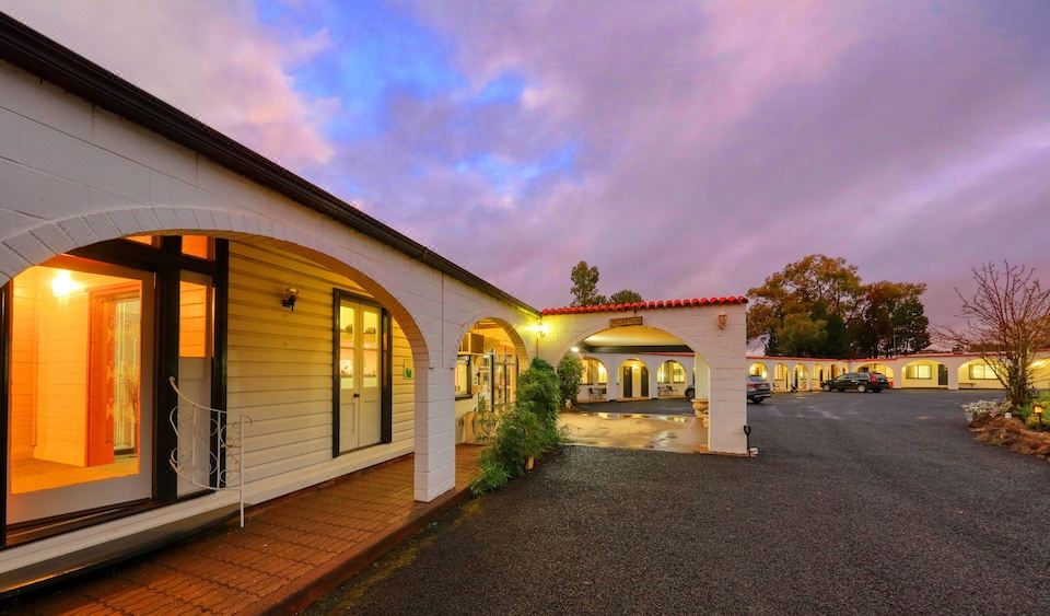 a white building with a red tile roof , surrounded by trees and a street at dusk at Azalea Motel