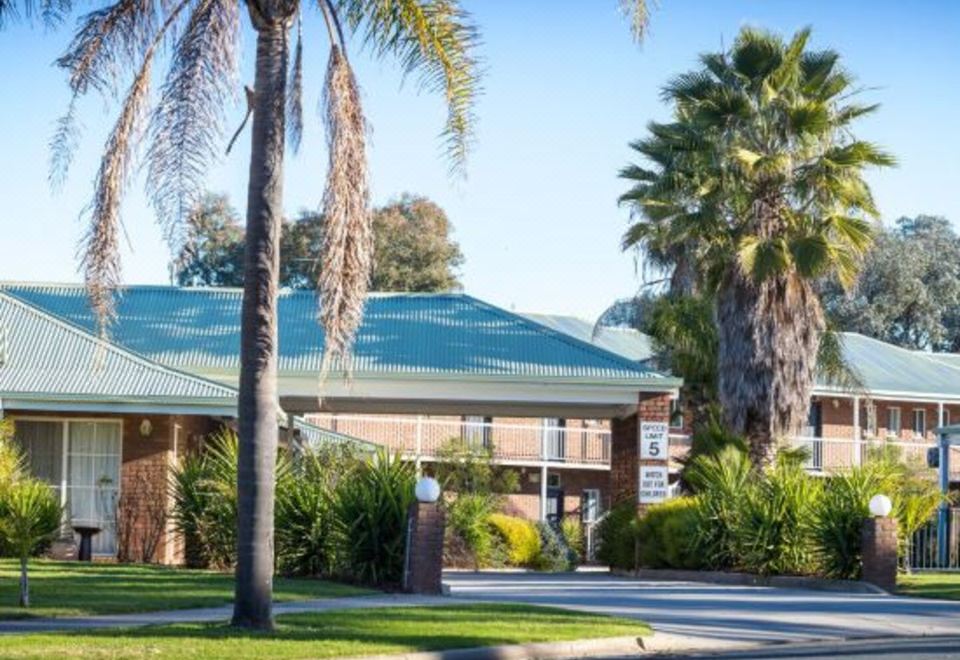 a building with palm trees and a sign in front of it , surrounded by grass and trees at Thurgoona Country Club Resort