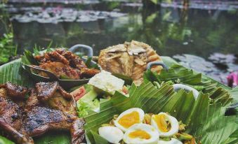 a large bowl of food is placed on a table in front of a body of water at Imah Seniman