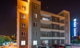 a modern apartment building with multiple balconies , illuminated by street lights at night , and cars parked in the lot at Prime Inn