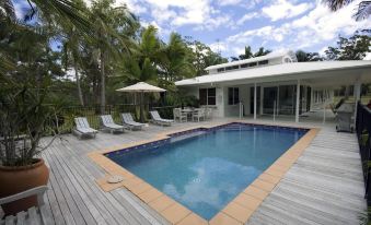 a large swimming pool is surrounded by a wooden deck and lounge chairs , with a white building in the background at Noosa North Shore Retreat