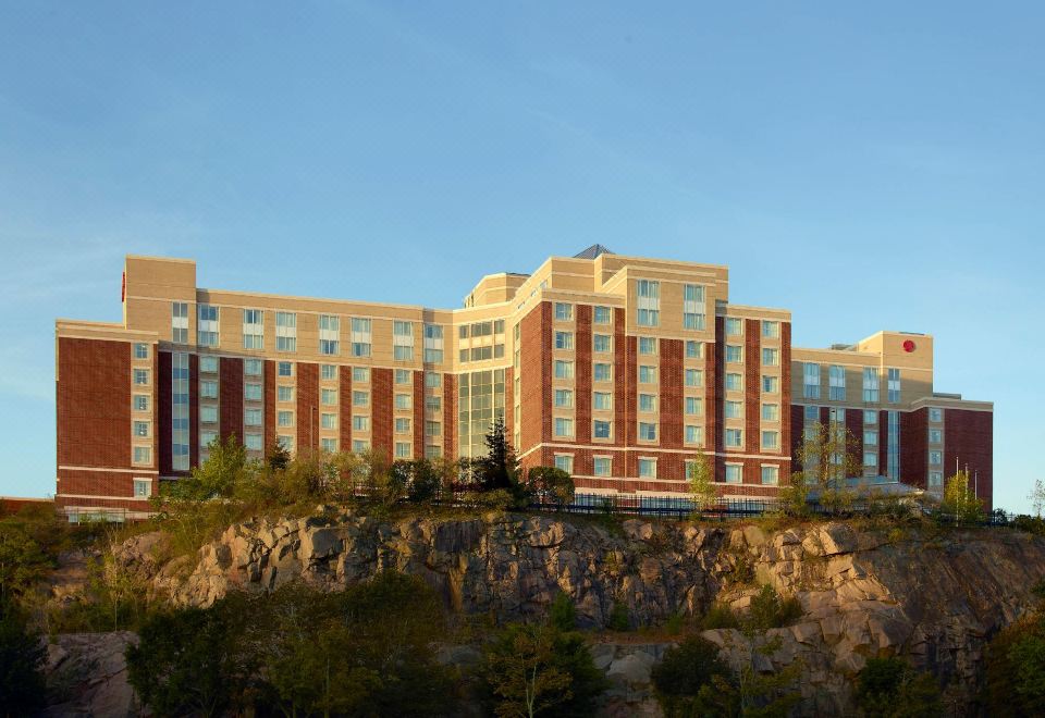 a large building with a red brick facade and white windows is situated on a rocky cliff at Marriott Boston Quincy