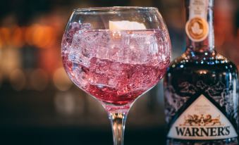 a wine glass filled with pink liquid is placed on a table next to a bottle of whiskey at Black Bull Hotel