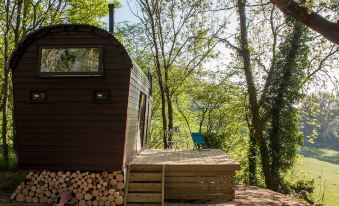 a small wooden house is nestled in a forested area with a deck and chair nearby at Extraordinary Huts Ltd