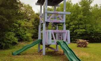 a wooden play structure with a green slide is set up in a grassy area at Savannah's Meadow