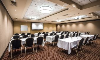 a large conference room with multiple tables and chairs , a projector screen , and a screen on the wall at Mercure Sydney Bankstown