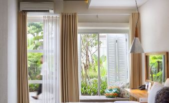 a bedroom with a bed , white curtains , and a window that has some plants outside at Yats Colony