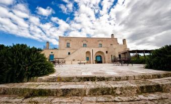 a large stone building with a courtyard in front of it , surrounded by chairs and tables at Masseria le Fabriche