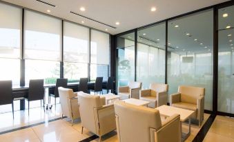 a modern waiting room with beige chairs and tables , surrounded by large windows and windows that offer views of the outdoors at Dormy Inn Mishima