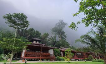 a traditional wooden house with a red roof , surrounded by lush greenery and misty mountains at Phuphayot Resort