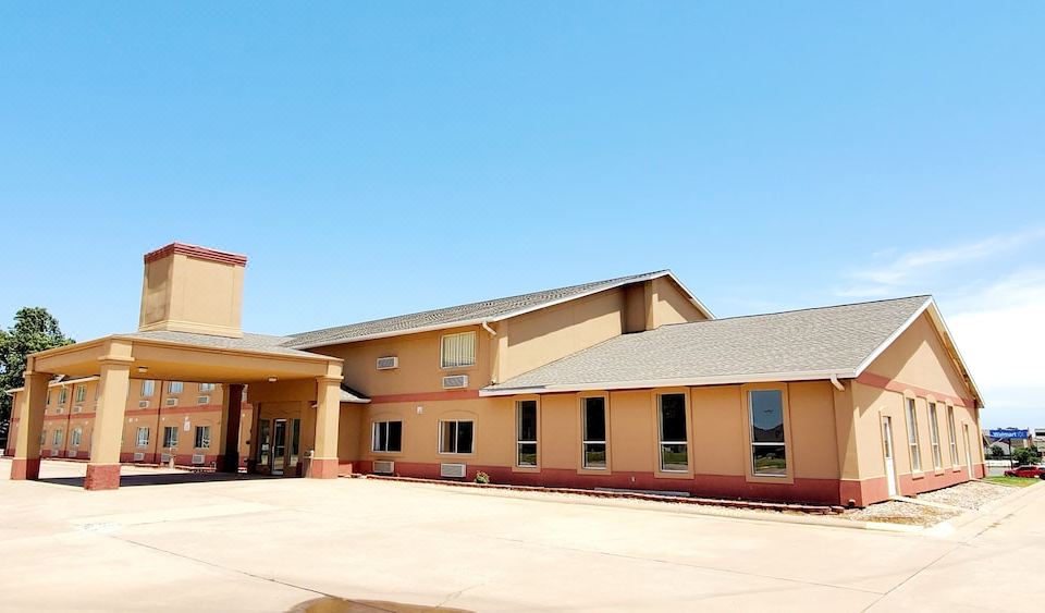 a large building with a tan exterior and a red roof , situated in an open parking lot under a clear blue sky at Executive Inn