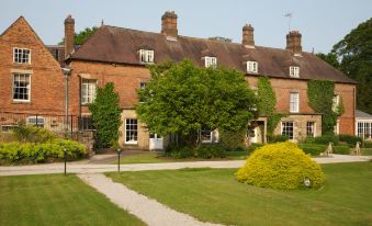 a brick house with a large tree in front of it , surrounded by green grass and bushes at Risley Hall Hotel