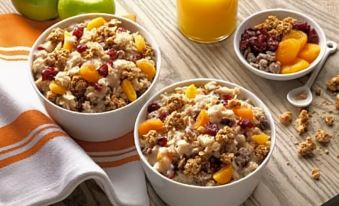 a wooden dining table with two bowls of oatmeal , each containing a different type of granola at Home2 Suites by Hilton Lawrenceville Atlanta Sugarloaf