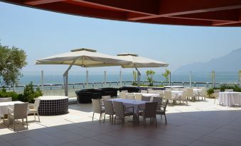 a patio with white tables and chairs , umbrellas , and a view of the ocean in the background at Grand Hotel Salerno
